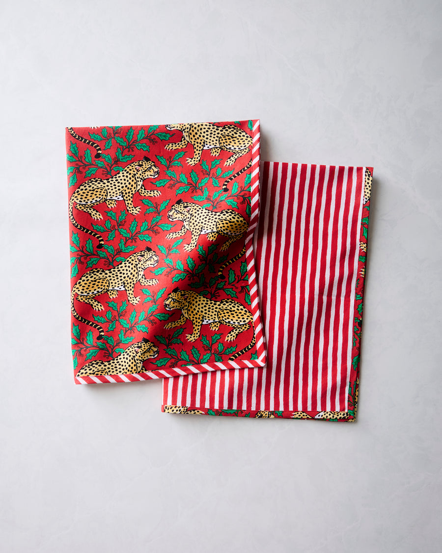Two folded Winter Holly Bagheera tea towels showing the leopard-and-holly print on one side and red-and-white stripes on the other.