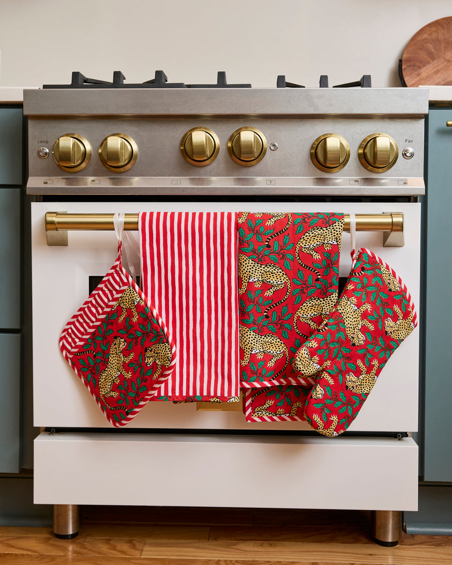 Two red patterned tea towels and a matching oven mitt hanging from a range handle.