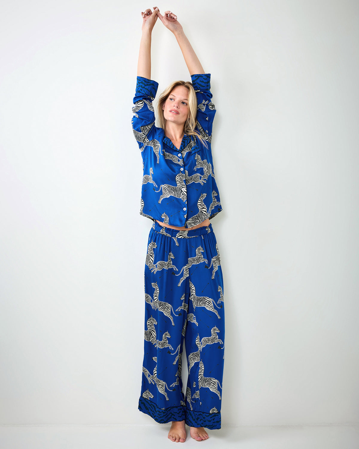 Person stretching while wearing a blue zebra-print pajama shirt and wide-leg pants.