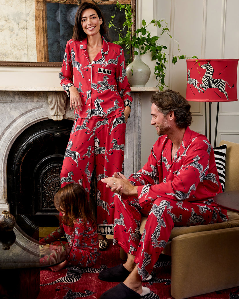 Two adults and a child wearing matching red zebra-print pajama sets in a living room.