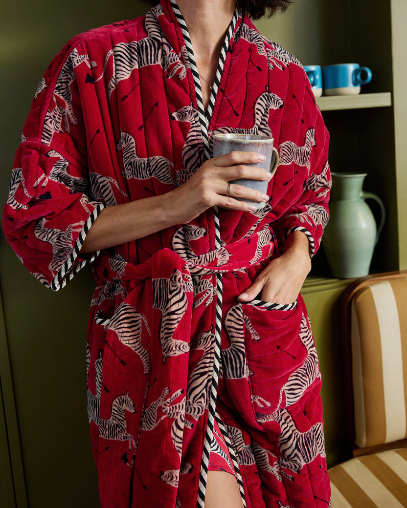 Close view of a red zebra-print quilted robe showing the shawl collar, belt, trim, and pocket.