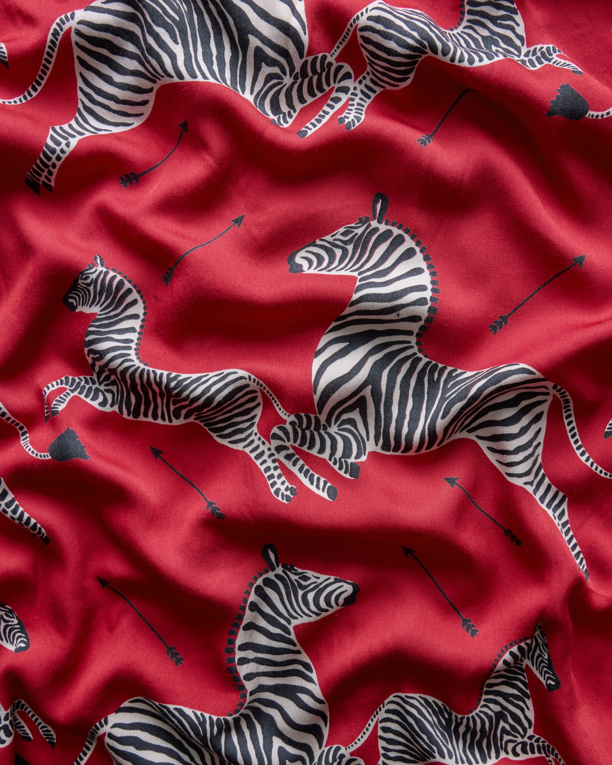 Close-up of red eco satin fabric with repeated black-and-white zebra and arrow prints.