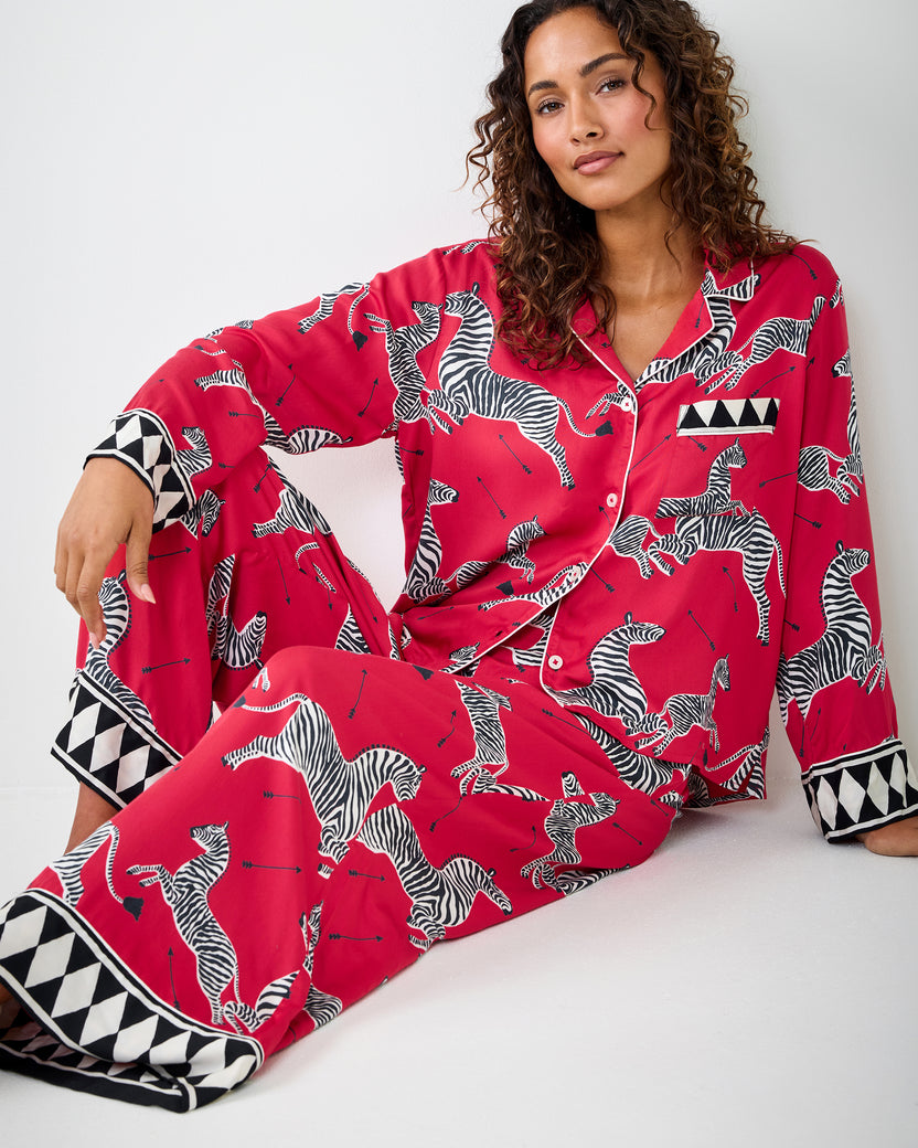 Person seated on the floor wearing the red zebra-print pajama set with geometric-trim cuffs and hems.