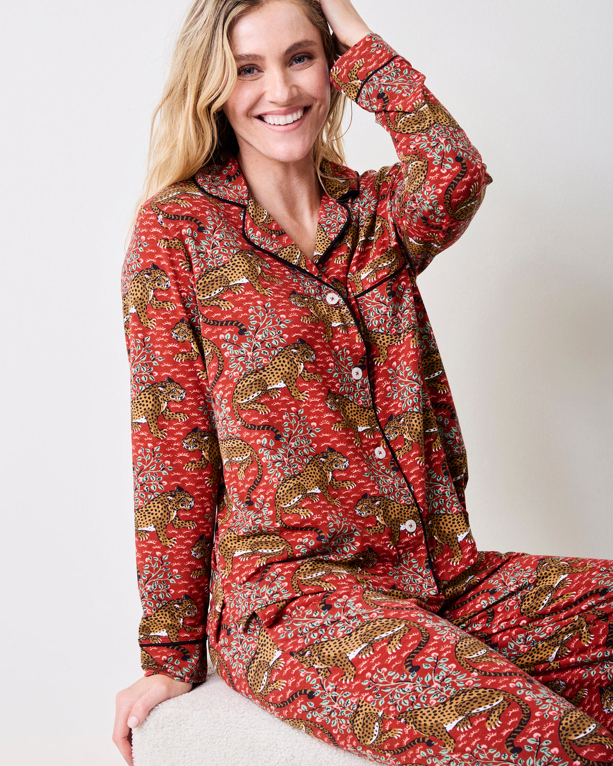 Person seated wearing the scarlet Bagheera long pajama set with a button-front long-sleeve top and matching leopard print pants.