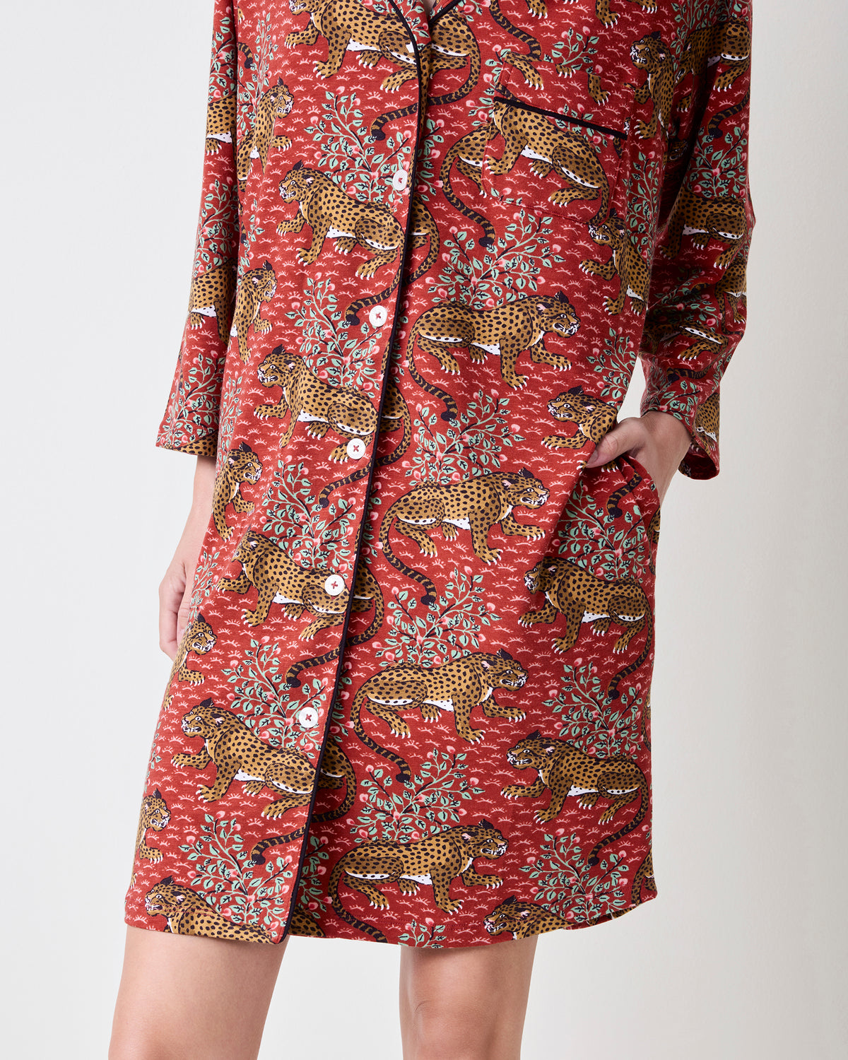 Front lower view of the Scarlet Bagheera sleep shirt showing its leopard and botanical print, buttons, black piping, hem, and side pocket.