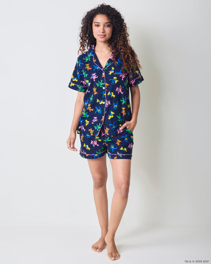 Front view of a person wearing a navy short pajama set with a multicolor dancing-bear print, button-front top, and matching shorts with pockets.