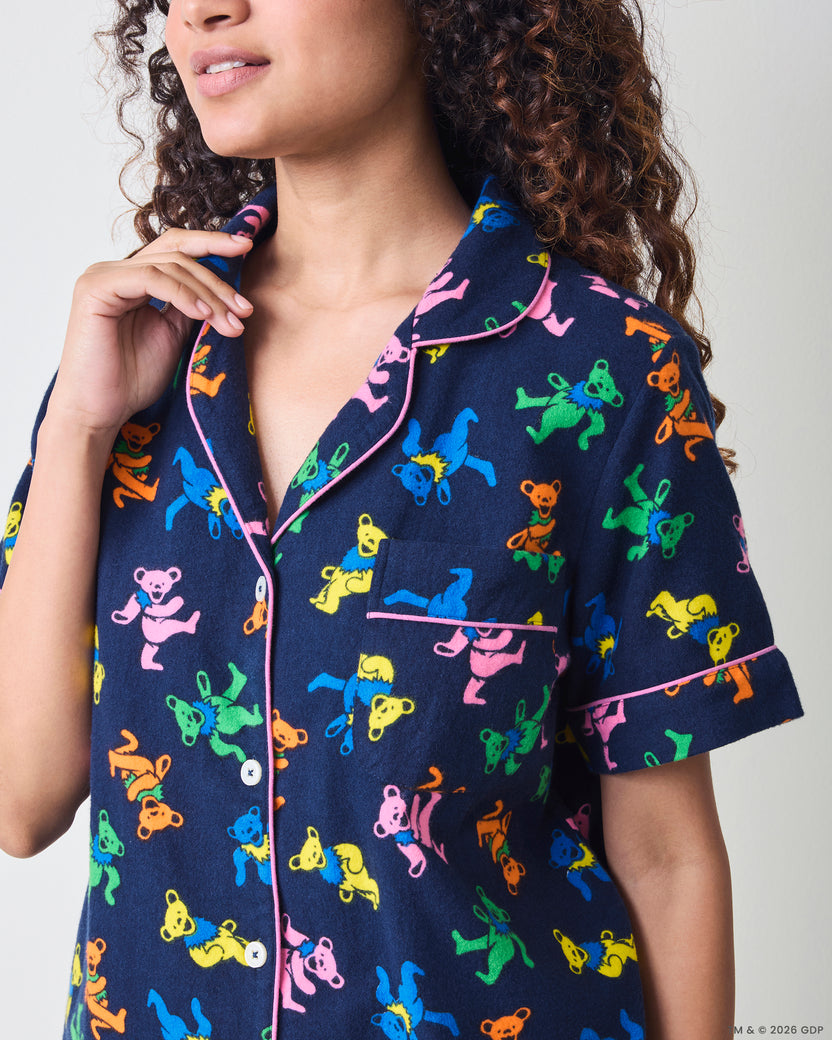Close view of the short navy pajama top with a multicolor dancing-bear print, pink piping, buttons, collar, and chest pocket.