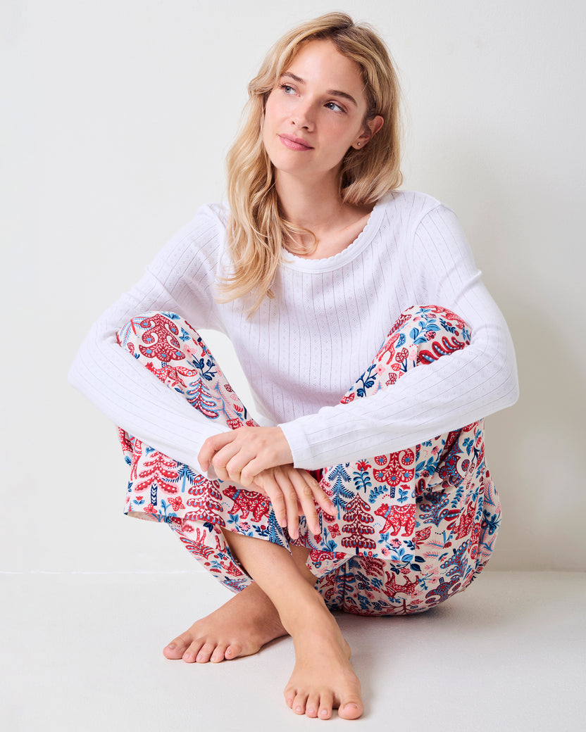 Adult model seated wearing cream Folklore Forest printed pajama pants with a white sweater.