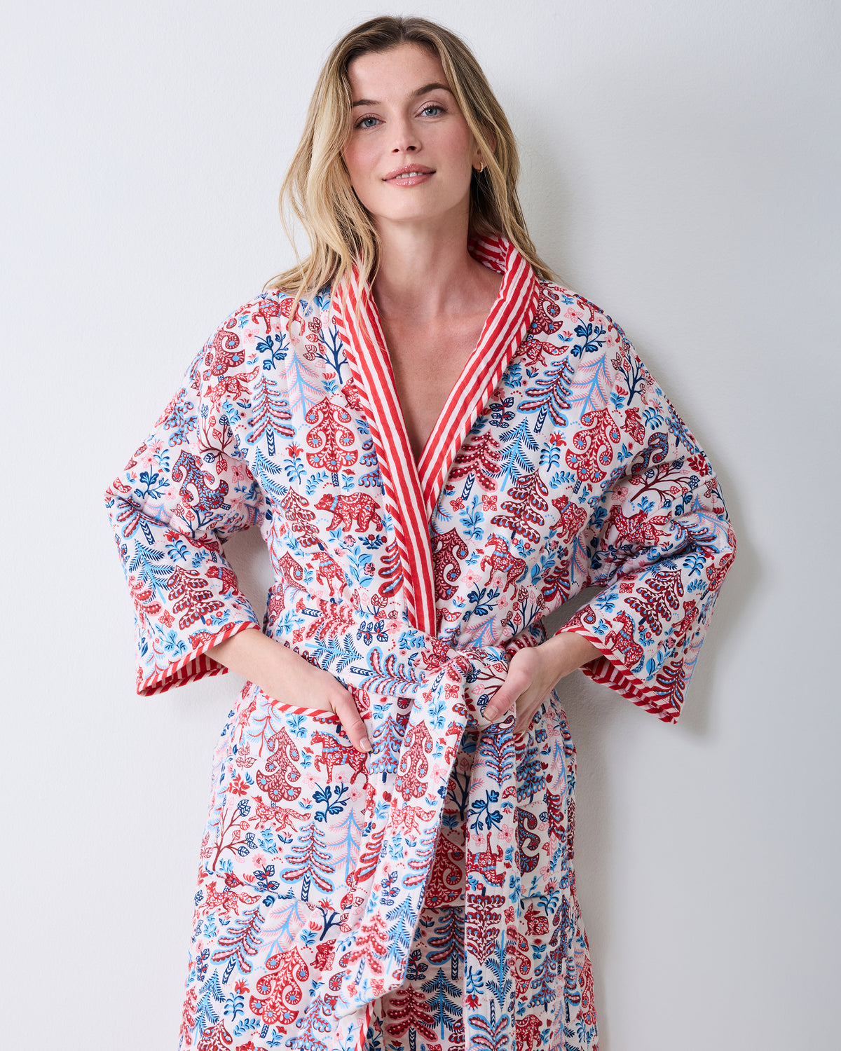 Front view of a cream reversible quilted robe with a red and blue forest-inspired print, striped trim, and tie belt.