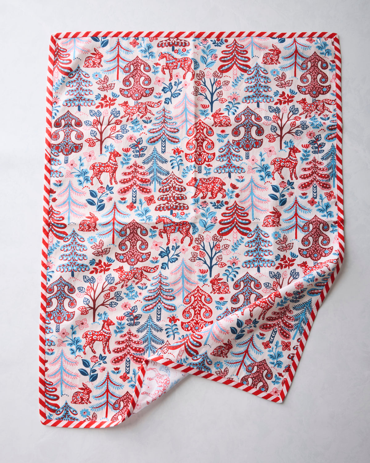 Tea towel showing the Folklore Forest pattern of trees, deer, and decorative motifs, with a striped border.