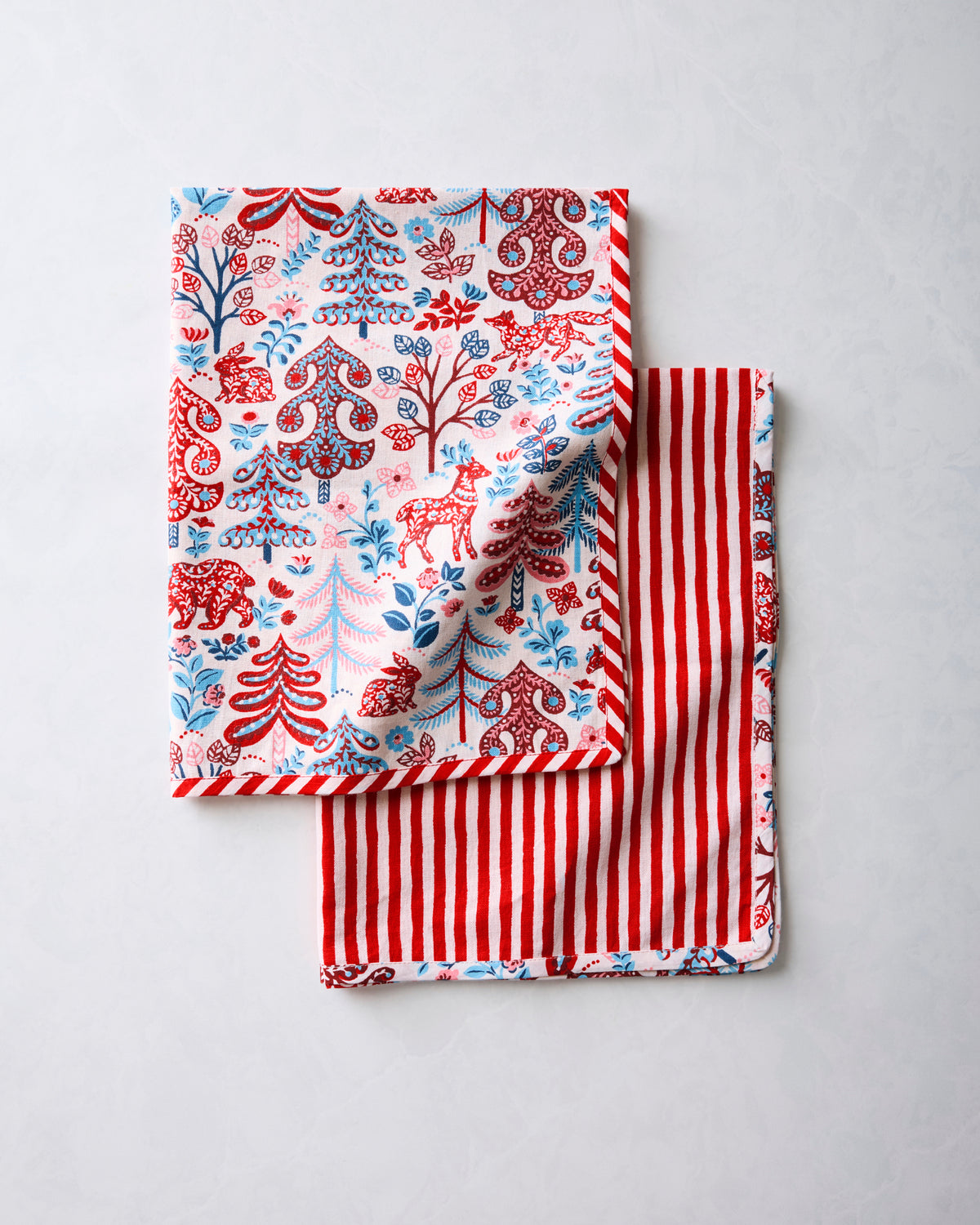 Two tea towels folded together, showing the patterned print and red-and-white striped reverse side.