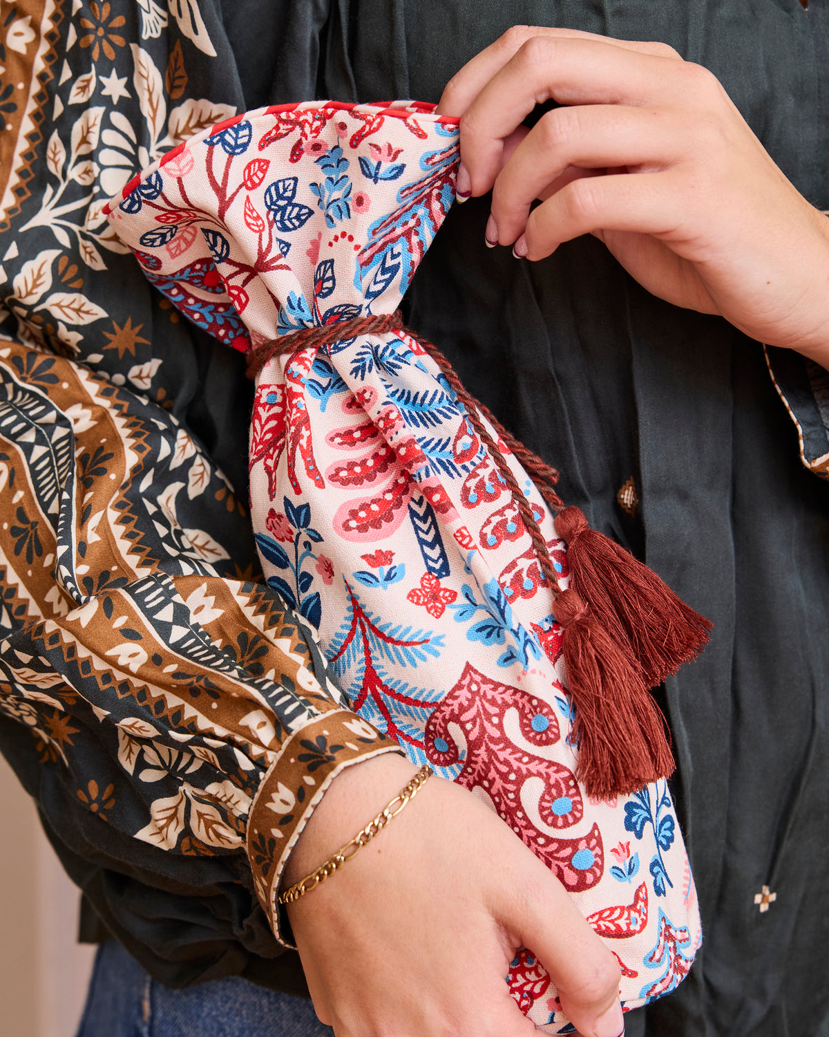 Cream Folklore Forest wine bag with a red-and-blue woodland print, held at the top and gathered with brown tassel ties.