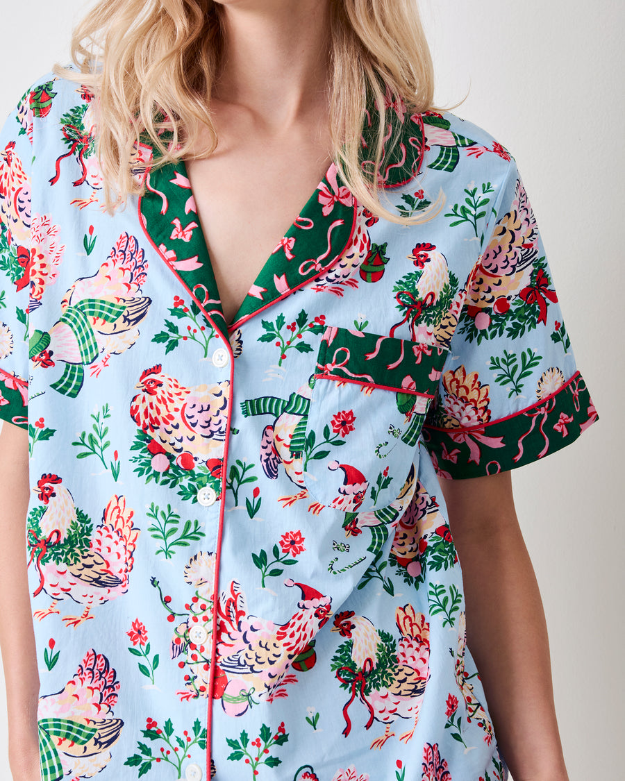 Close-up of the pale blue Holiday Hens pajama top showing its printed hens, floral motifs, collar, buttons, pocket, and contrasting trim.