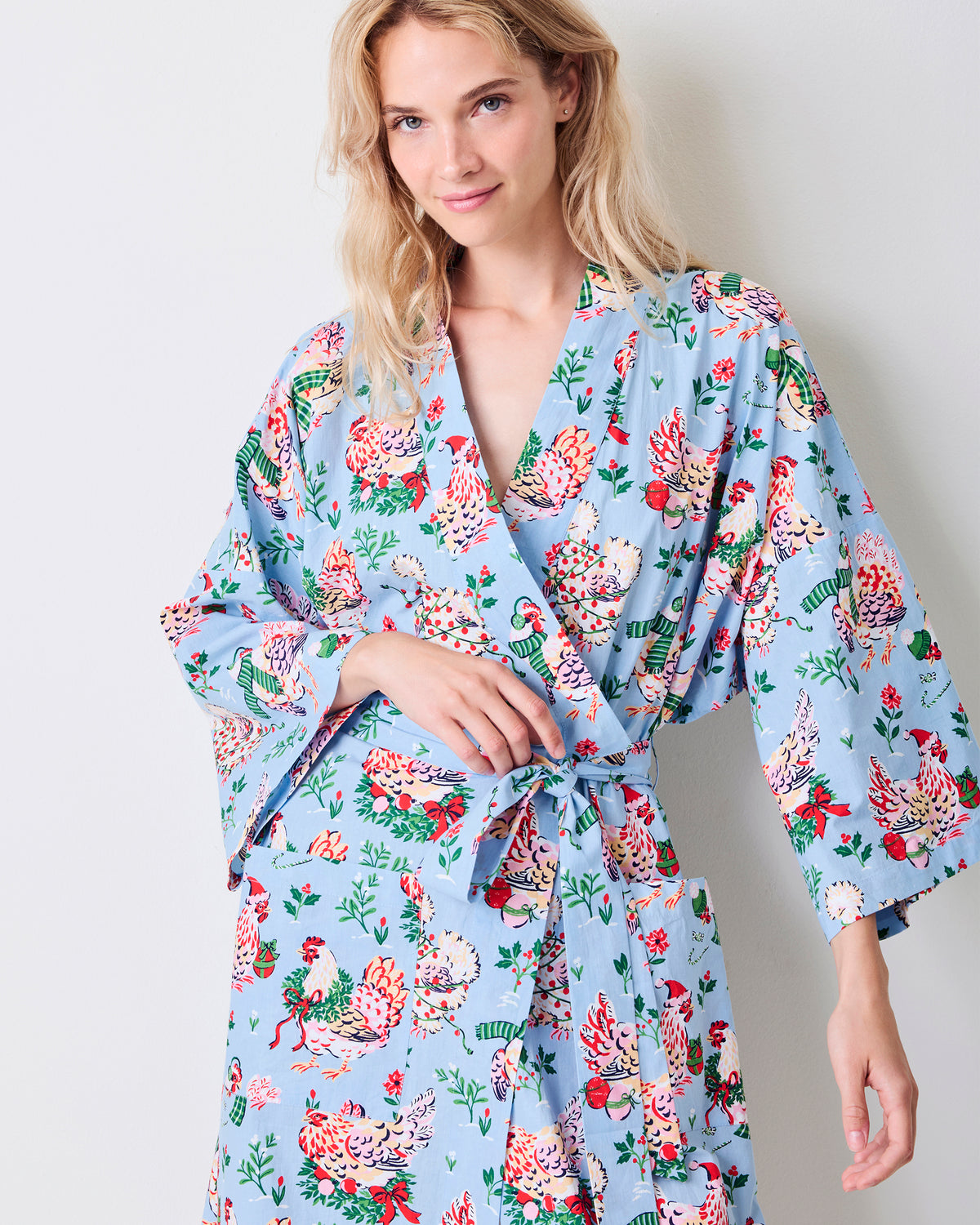 Close-up front view of the pale blue Holiday Hens robe with wide sleeves, a tied belt, and a print of hens wearing winter hats and scarves.