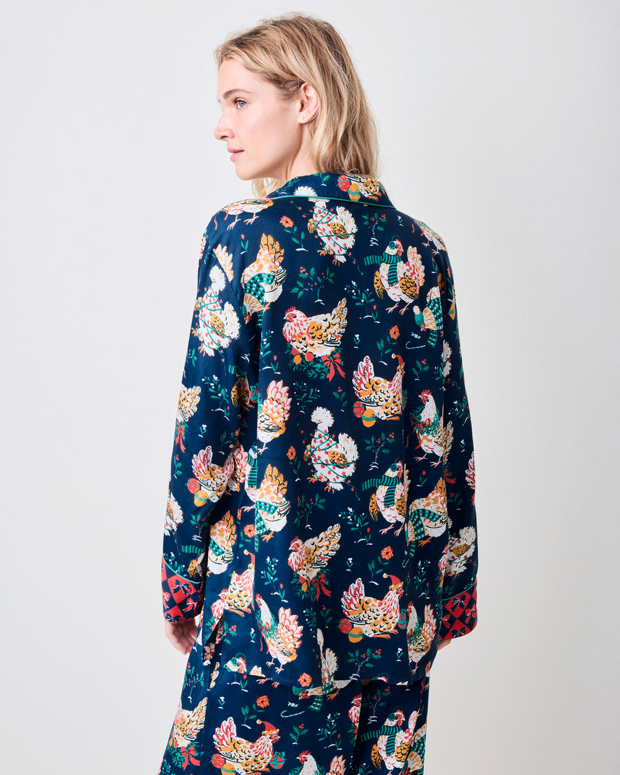 Back view of a model wearing a navy pajama set with festive hen print and red patterned cuffs.