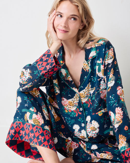 Model seated in a navy chicken-print tunic pajama set with a long button-front top and wide-leg pants.