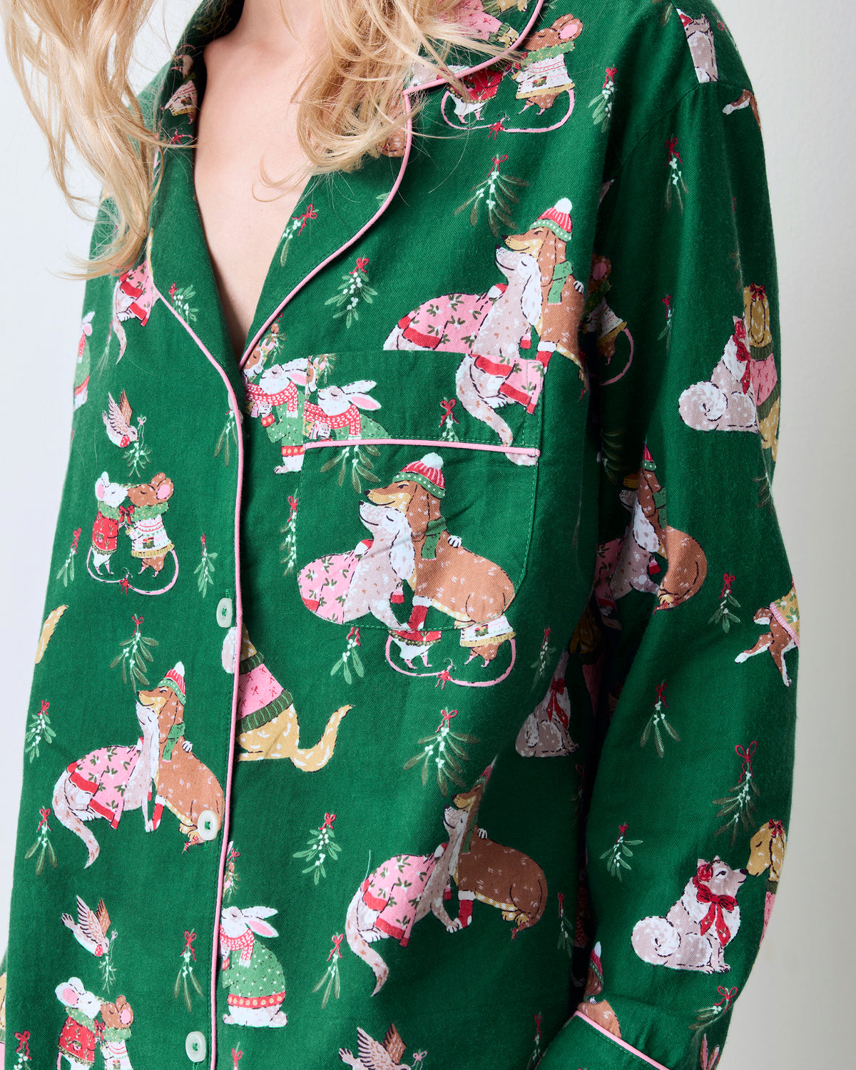 Close view of the green Mistletoe Kiss pajama top showing pink piping, button closure, chest pocket, and holiday critter print.
