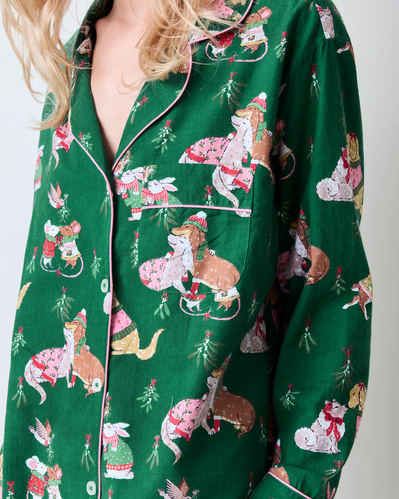 Close view of the green Mistletoe Kiss pajama top showing pink piping, button closure, chest pocket, and holiday critter print.