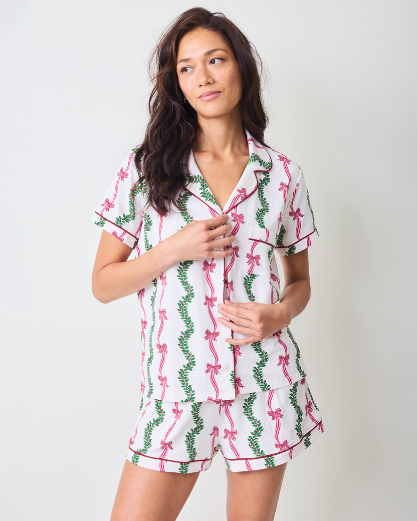 Model wearing the Ribbons & Bows short pajama set with a button-front top and matching shorts in a pink bow and green garland print.