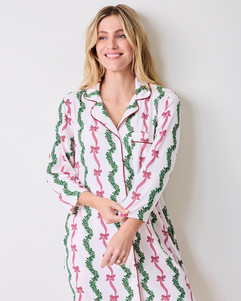 Model wearing a long-sleeved button-front sleep shirt with a pink bow and green vine print on a light background.