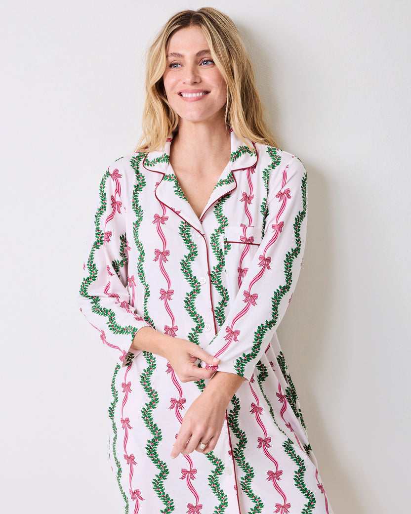 Model wearing a long-sleeved button-front sleep shirt with a pink bow and green vine print on a light background.
