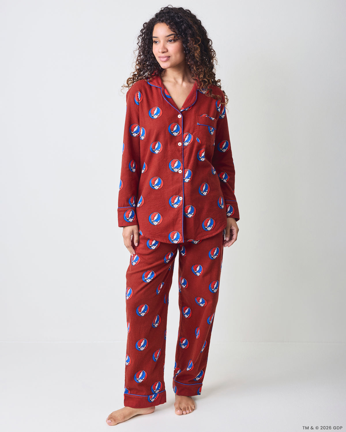Person wearing a long-sleeved button-front pajama top and matching pants with a red print of circular blue-and-white lightning-bolt motifs.