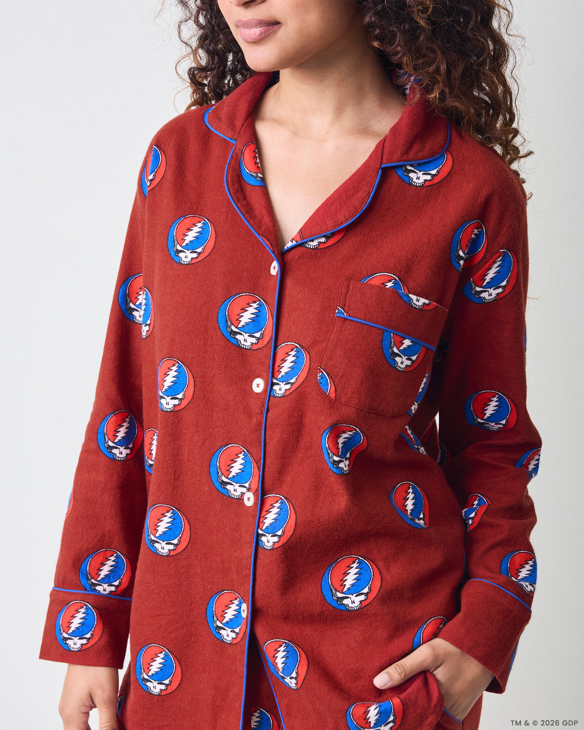 Front close-up of a red long-sleeve pajama top with blue piping, a chest pocket, and a repeated skull-and-lightning-bolt print.