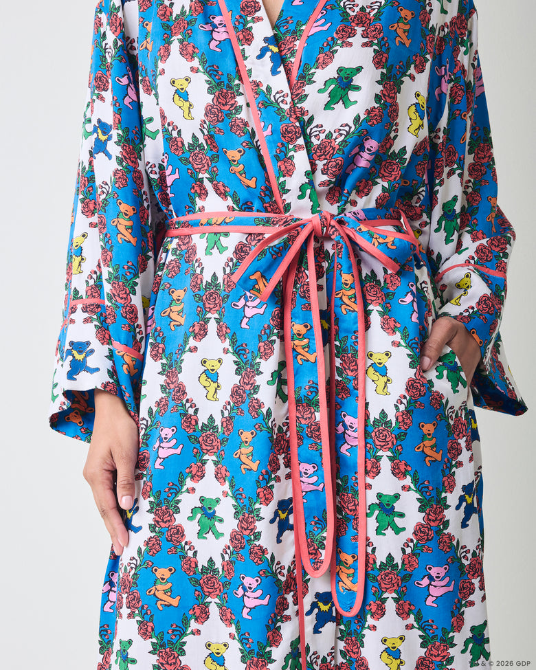 Close front detail of a robe showing the pink waist ties, trim, sleeves, and side pocket with a blue-and-white bear-and-rose print.