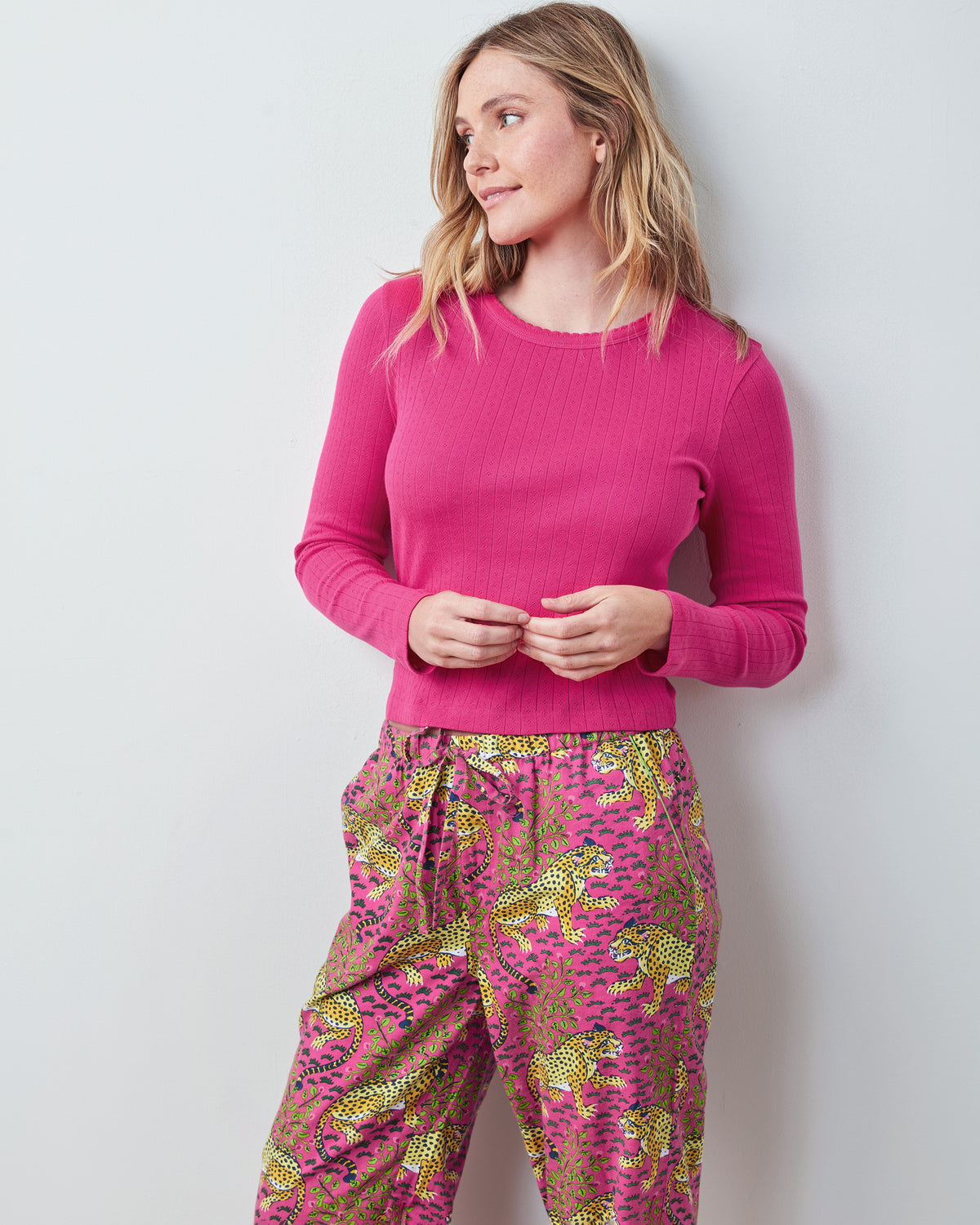 Bright pink long-sleeve pointelle shirt shown from the front with hands at the waist