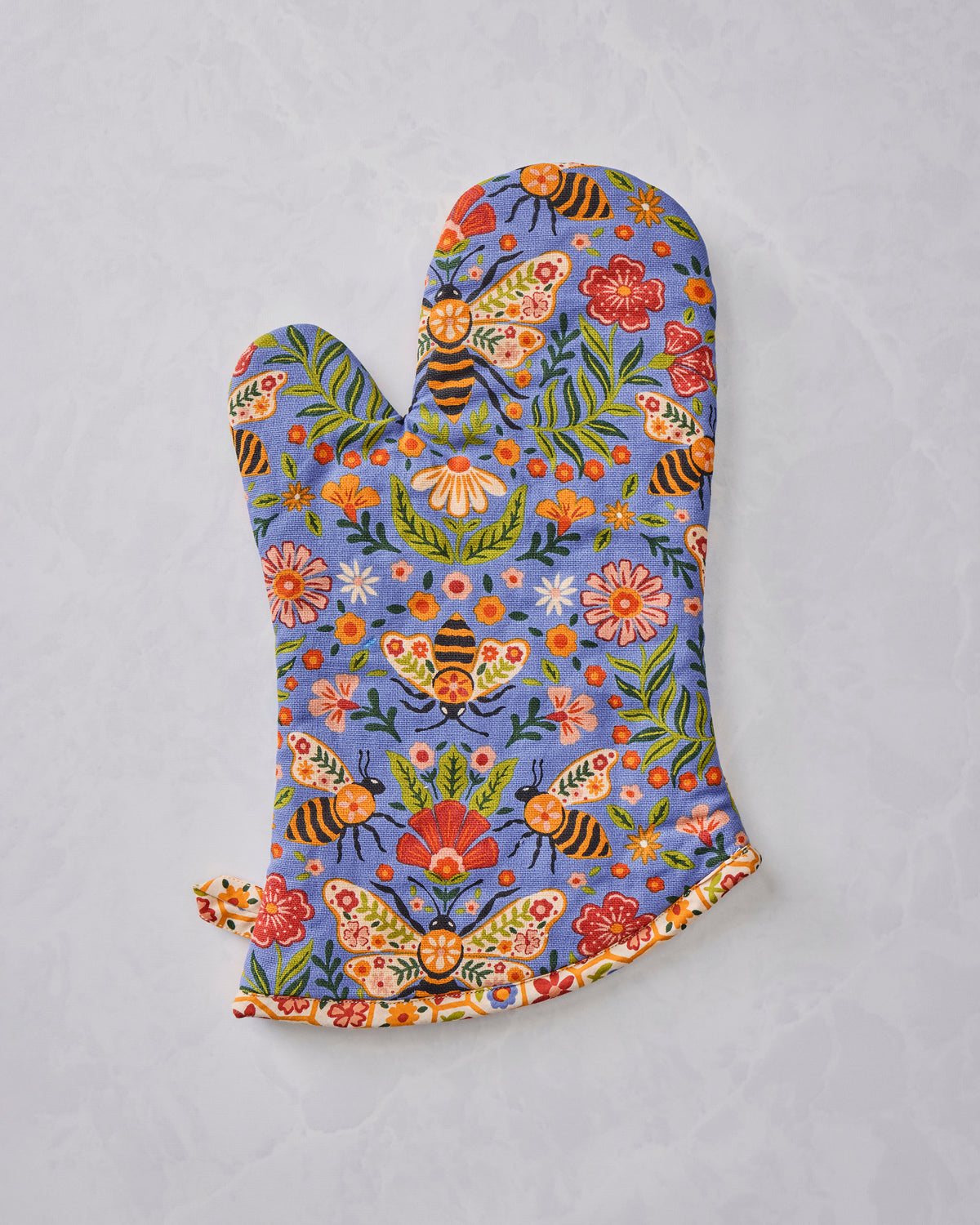 Reverse-side view of a blue floral oven mitt with bee, butterfly, flower, and leaf print.