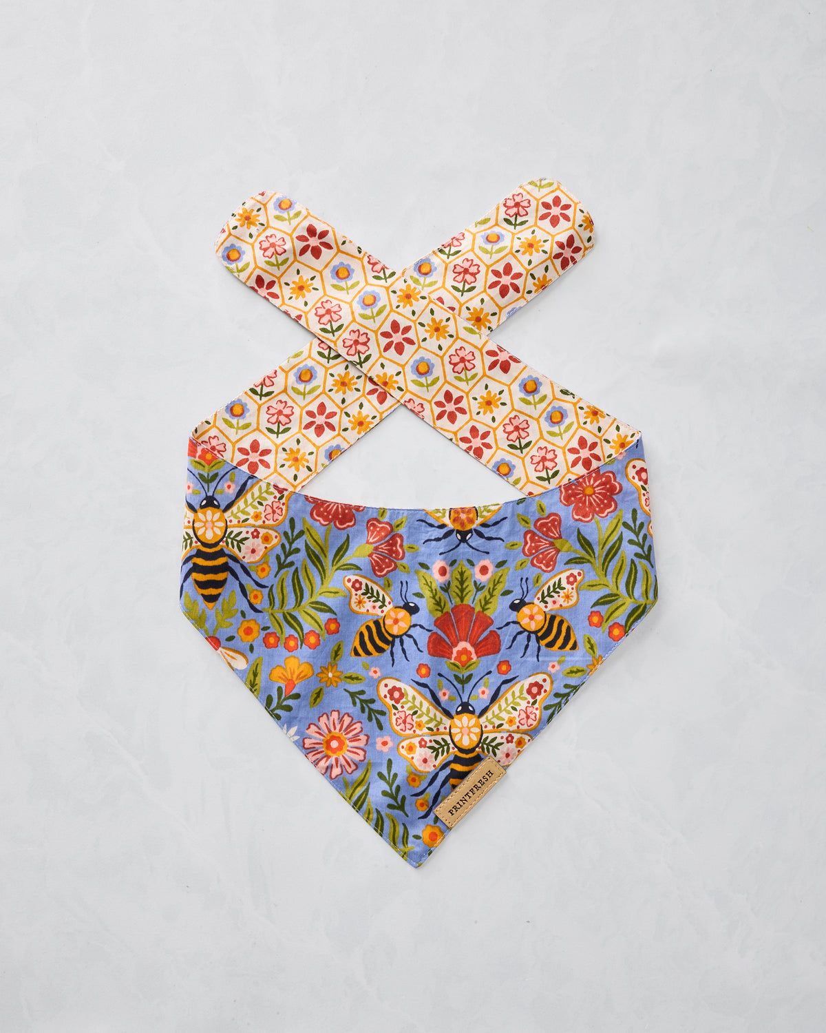Bee Tapestry pet bandana in Delphinium Blue, shown flat with a floral bee print and patterned neck ties.
