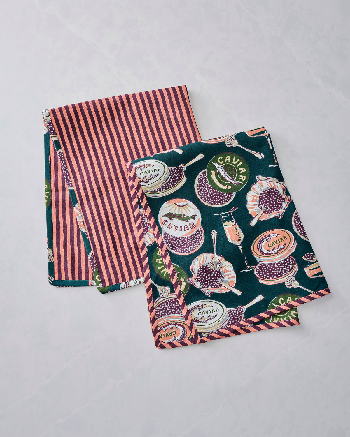 Two Champagne & Caviar tea towels displayed together, showing the printed side and pink-and-brown striped side.