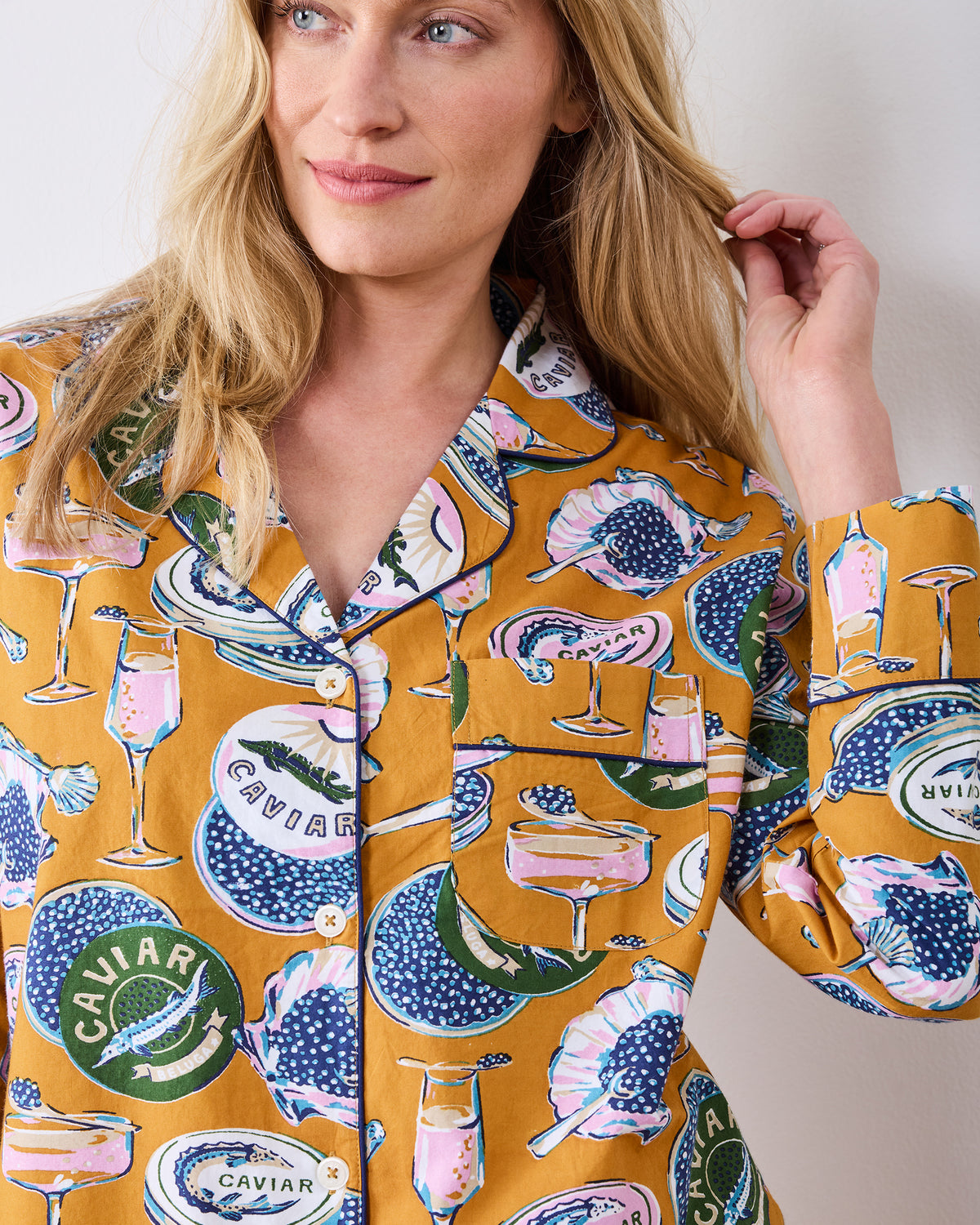 Close view of the goldenrod Champagne & Caviar pajama top, showing its notched collar, button front, chest pocket, and champagne-and-caviar print.