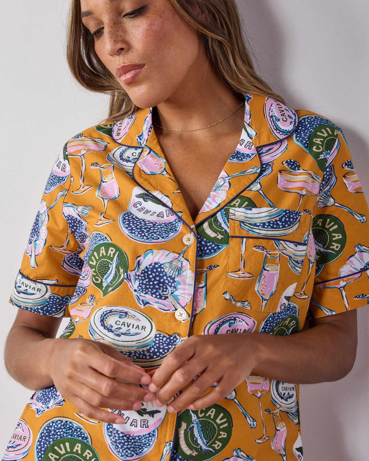 Close-up of the goldenrod pajama top showing its printed caviar and champagne motif, collar, buttons, and chest pocket.
