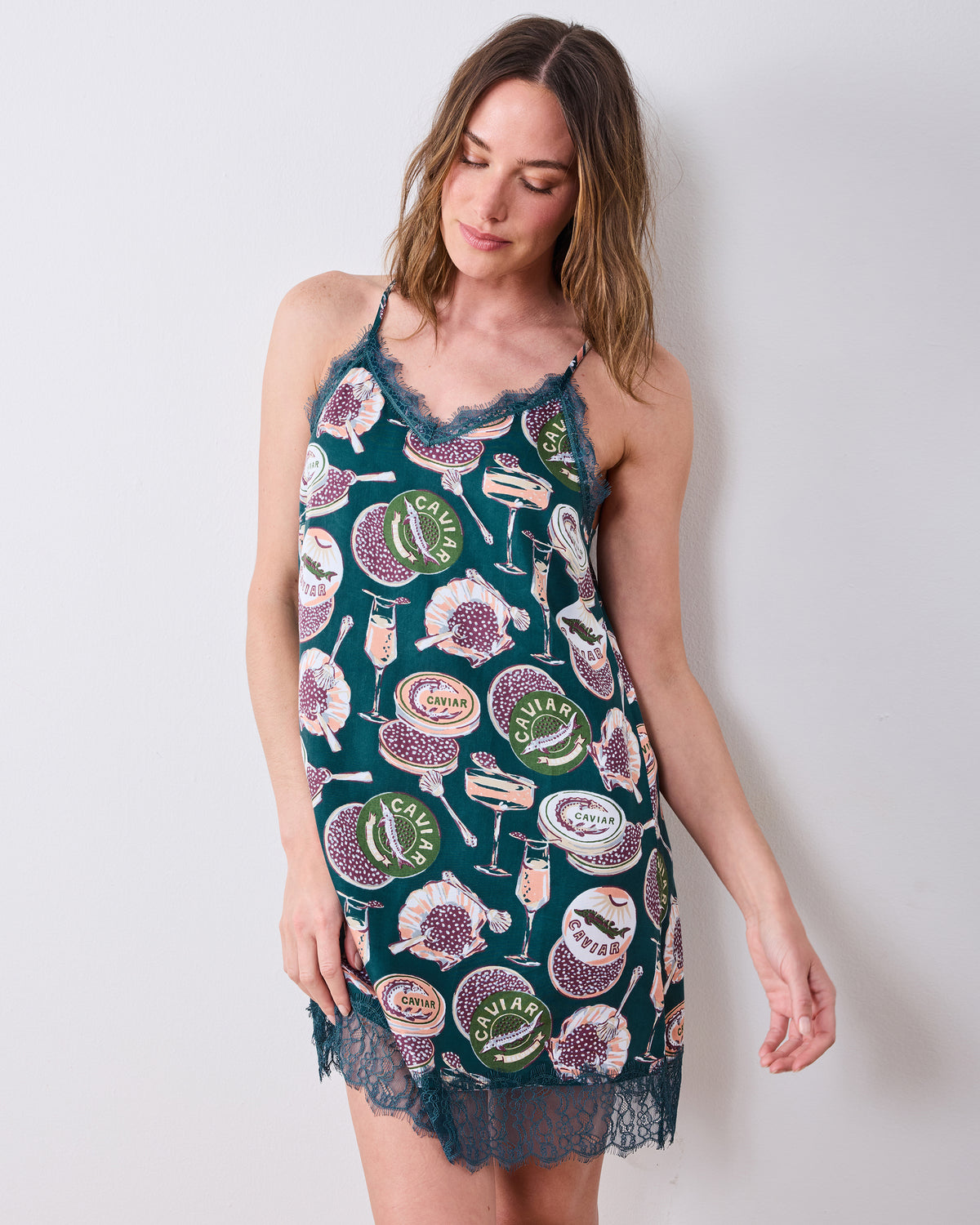 Front view of a short printed nightie with lace-trimmed straps and hem, featuring caviar tins, champagne flutes, and shells.