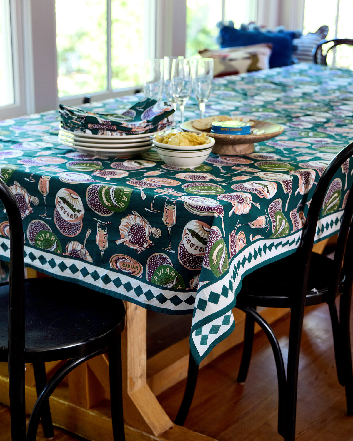Champagne & Caviar rectangular tablecloth covering a dining table set with plates, glasses, napkins, crackers, and a caviar tin.
