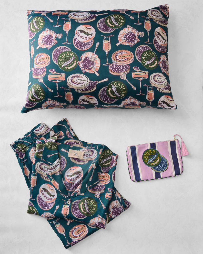 Champagne and caviar top shelf bundle arranged flat with a pillowcase, folded pajama set, and striped pouch.