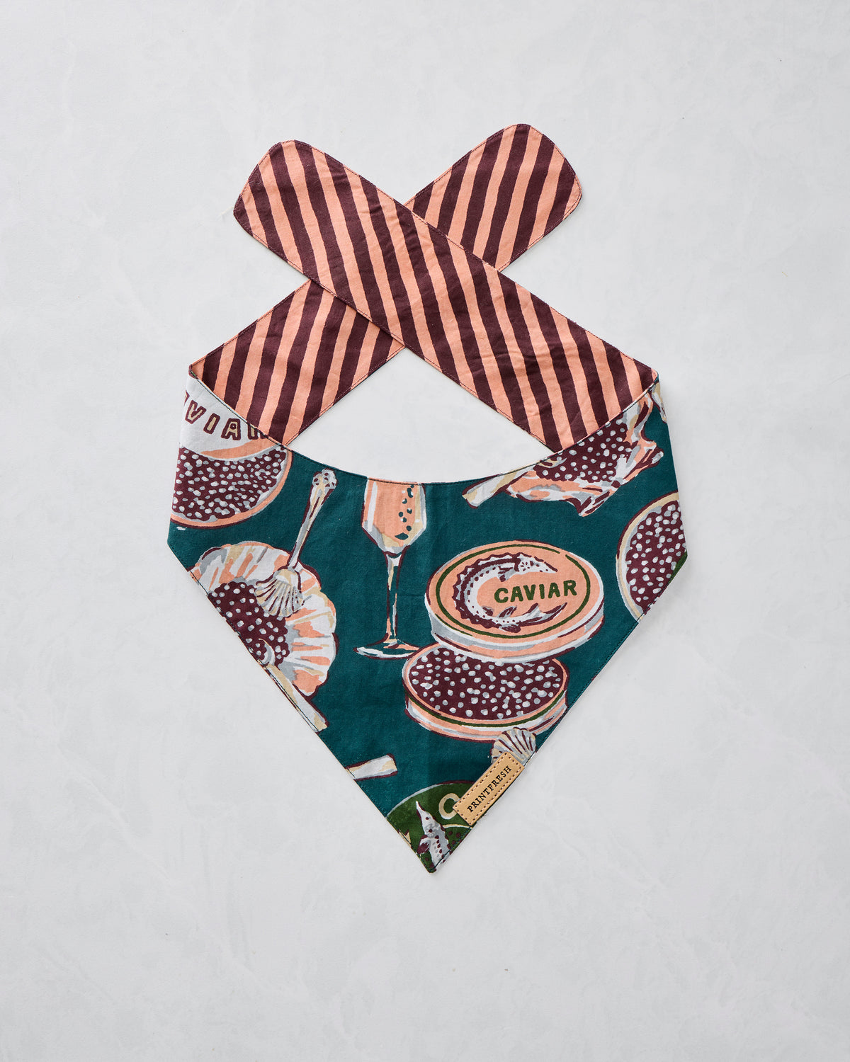 Single Champagne & Caviar pet bandana displayed flat with a teal caviar-themed print and striped tie straps.