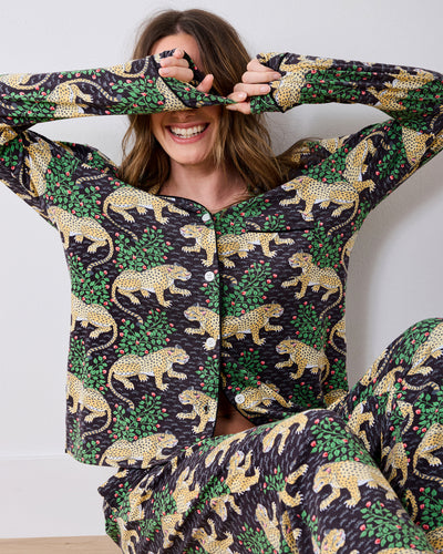 Person wearing a long-sleeve button-front pajama set with a leopard-and-leaf print, seated with hands covering the eyes.