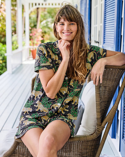 Person seated in a wicker chair on a porch wearing a black short pajama set with a leopard-and-floral print.