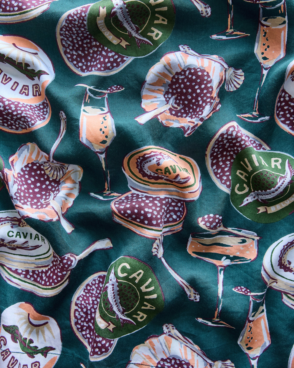 Close-up of the peacock-feather Champagne & Caviar print on a dark teal background, showing caviar tins, champagne glasses, spoons, fish, and shells.