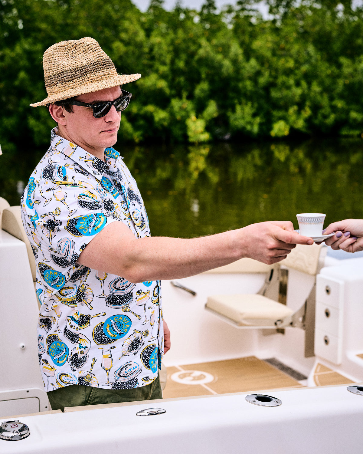 Side view of the Champagne & Caviar Leo Shirt worn on a boat, showing its printed caviar tin and champagne glass pattern.