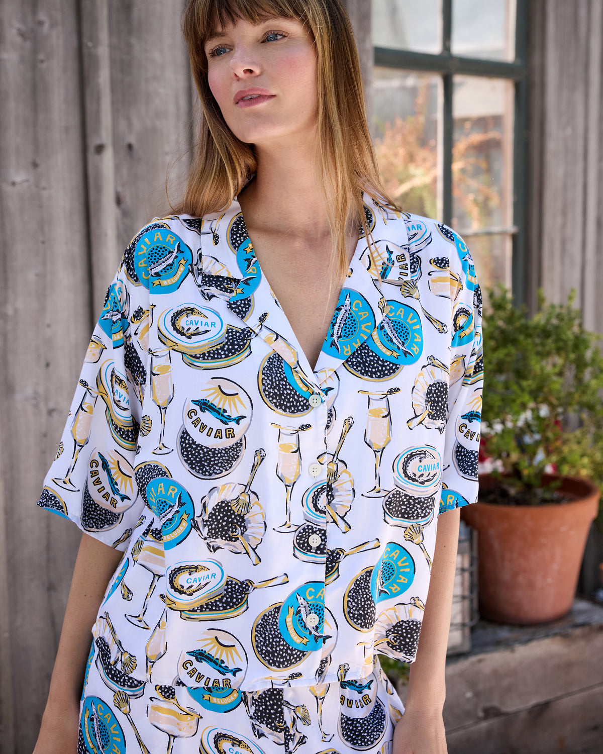 Close view of the Pearl pajama top with a notched collar, short sleeves, buttons, and champagne glass and caviar tin print.