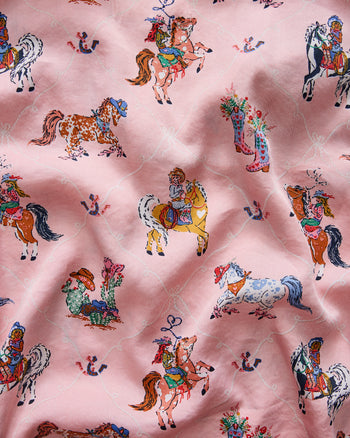 Close-up of the pink pajama fabric printed with horses, cowgirls, Western boots, horseshoes, and a pale diamond pattern.