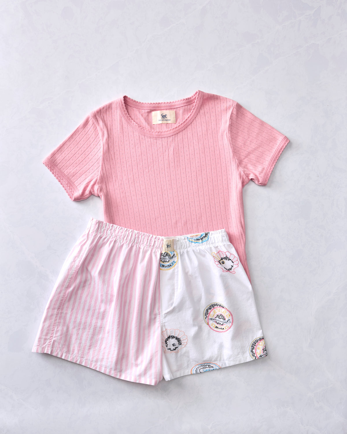 Flat lay of a pink ribbed short-sleeve shirt and white pajama boxer shorts with printed motifs.