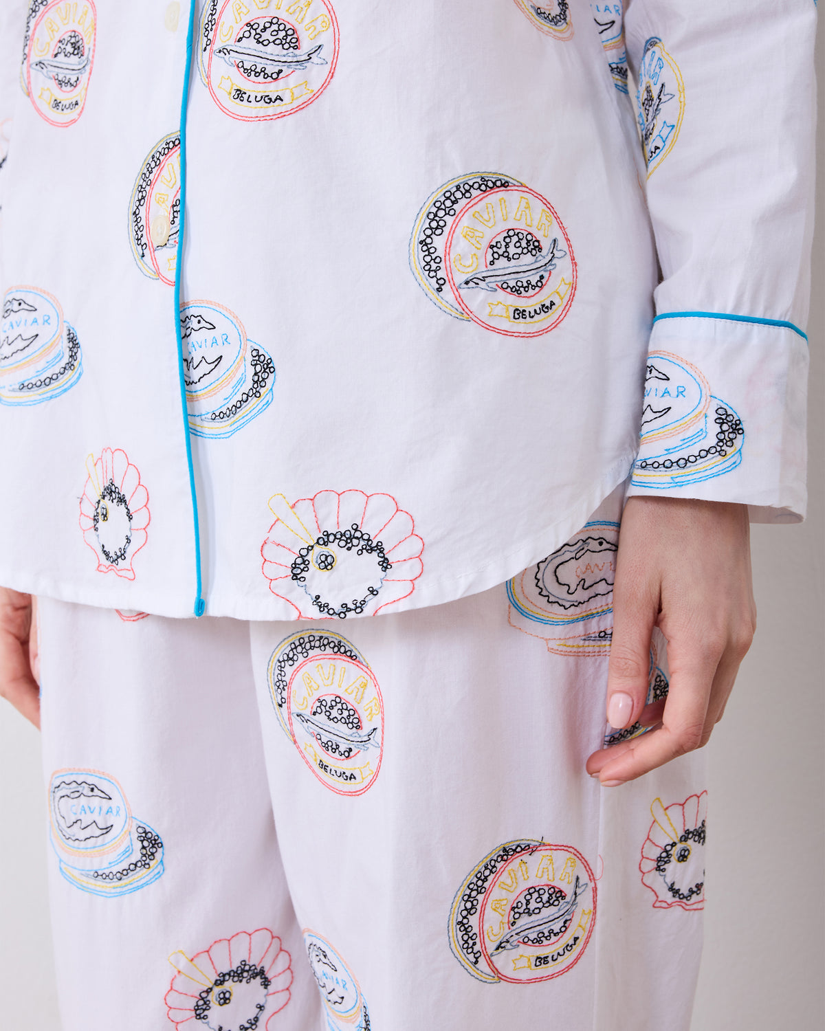 Close-up of the Embroidered Caviar Club long pajama set, showing the piped shirt cuff, shirt hem, and embroidered motifs on the shirt and pants.