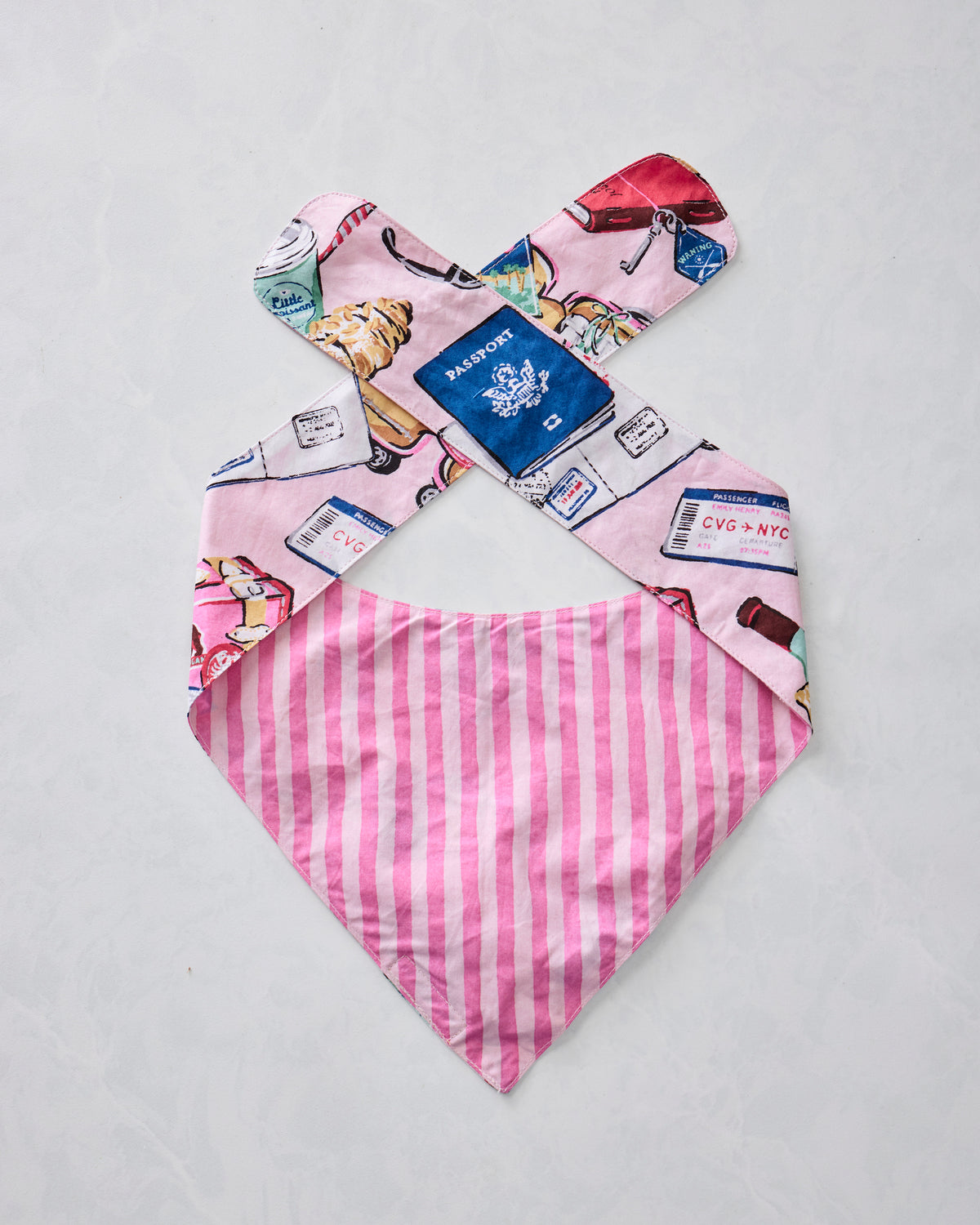 Reversible pet bandana showing the pink-and-white striped reverse and travel-themed printed side.