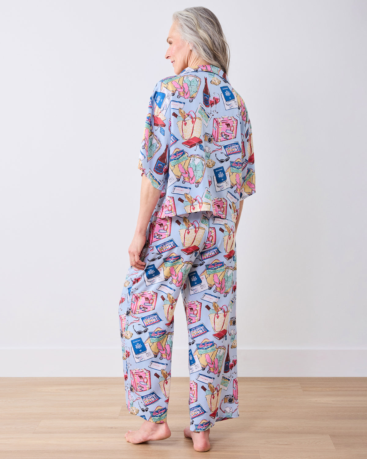 Back view of the pale blue Wildest Dreams pajama set with a button-down top and wide-leg pants featuring travel-themed illustrations.