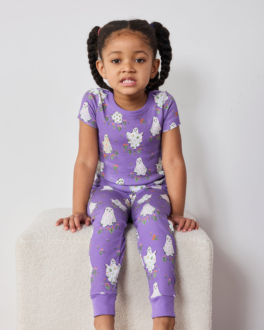 Child seated wearing a purple short-sleeve ghost-print pajama top and matching pants