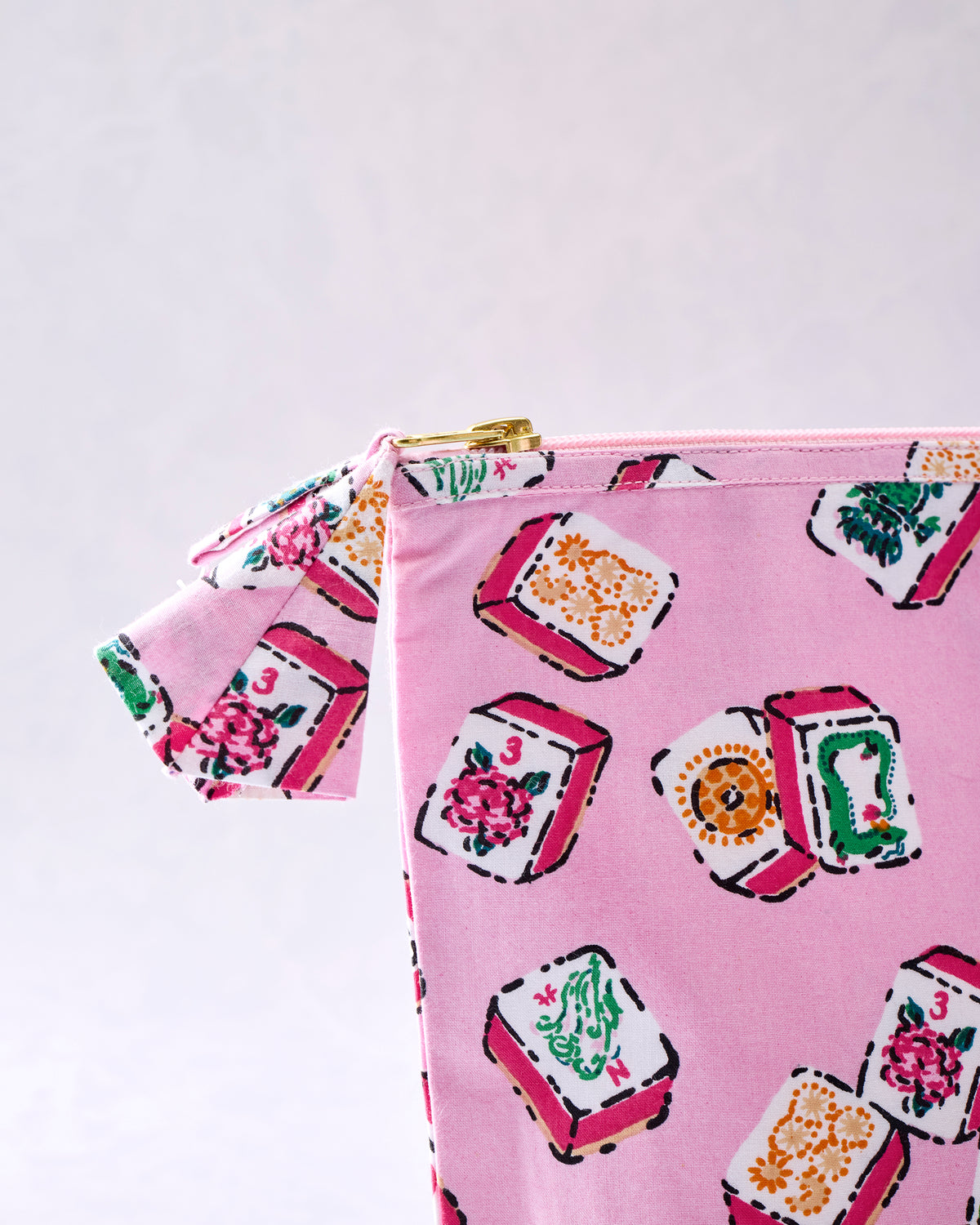 Close-up of the pink printed pouch showing its gold zipper, fabric pull tab, and tile-pattern design.